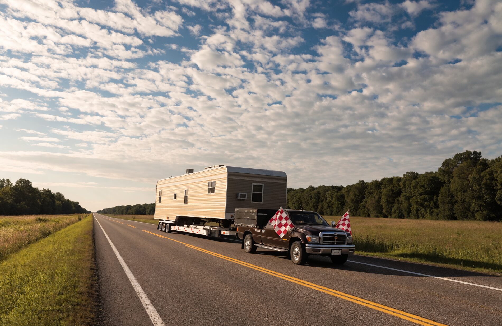 A manufactured home on a specialized trailer moving down a two-lane road at dawn